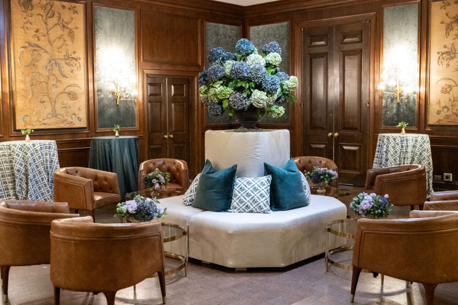 Elegant lounge area with brown leather chairs and a large floral centerpiece, reflecting 2025 wedding design trends.