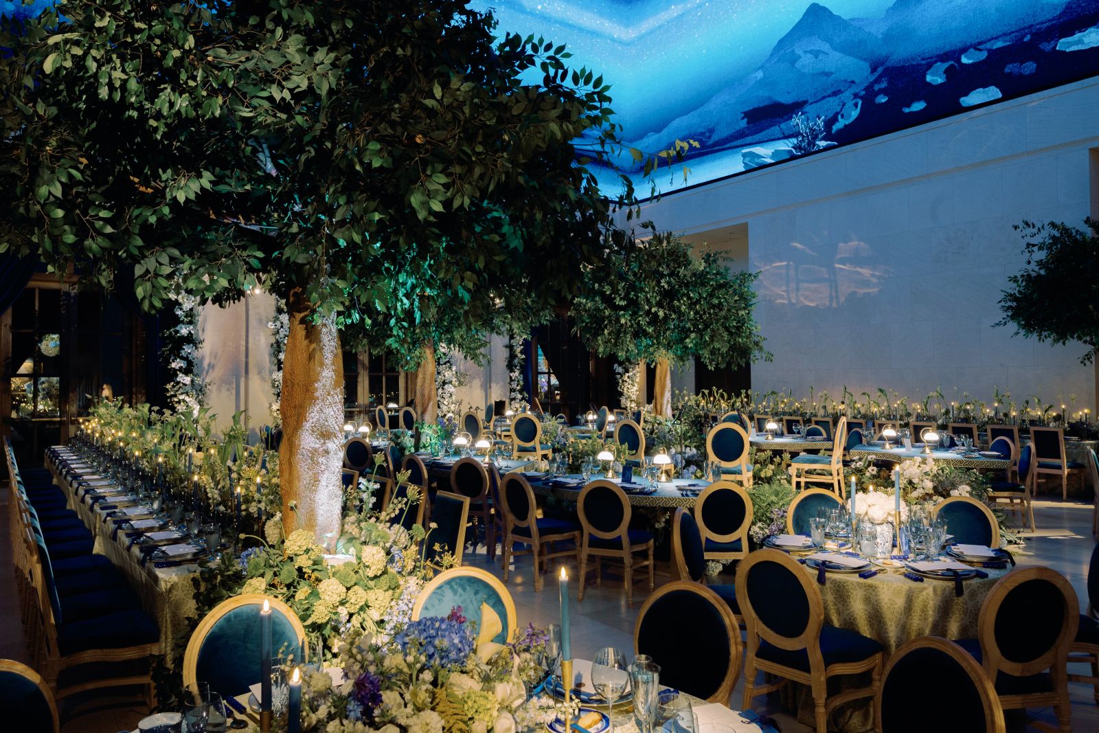 A grand wedding reception hall with trees, blue chairs, and a starry ceiling, showing 2026 wedding trend predictions.