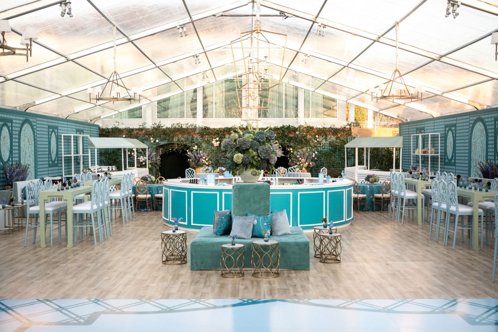 A large tented event space with teal and light green decor, tables, and a bar.