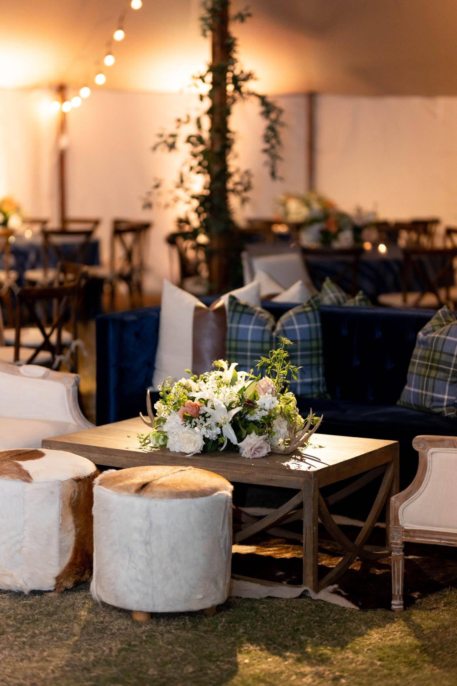 A cozy lounge area with a blue velvet couch, plaid pillows, and fur ottomans.